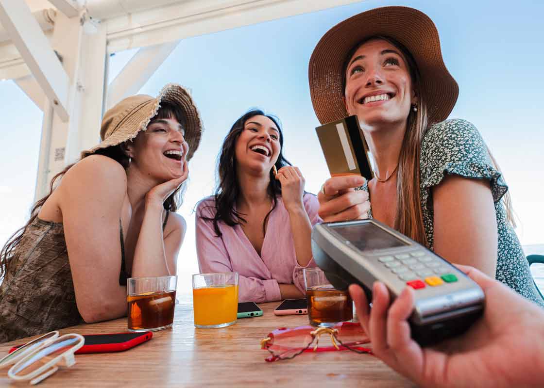 3 young women at a seaside cafe making credit card transaction on a portable card machine.